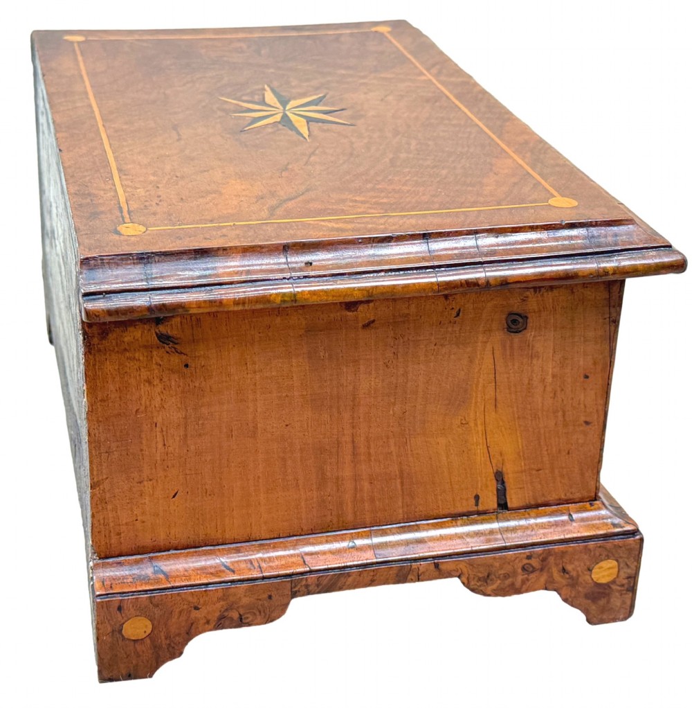 An early 18th-century walnut miniature chest featuring two drawers, star marquetry inlay, crossbanding, brass drop ring handles, and bracket feet. View V