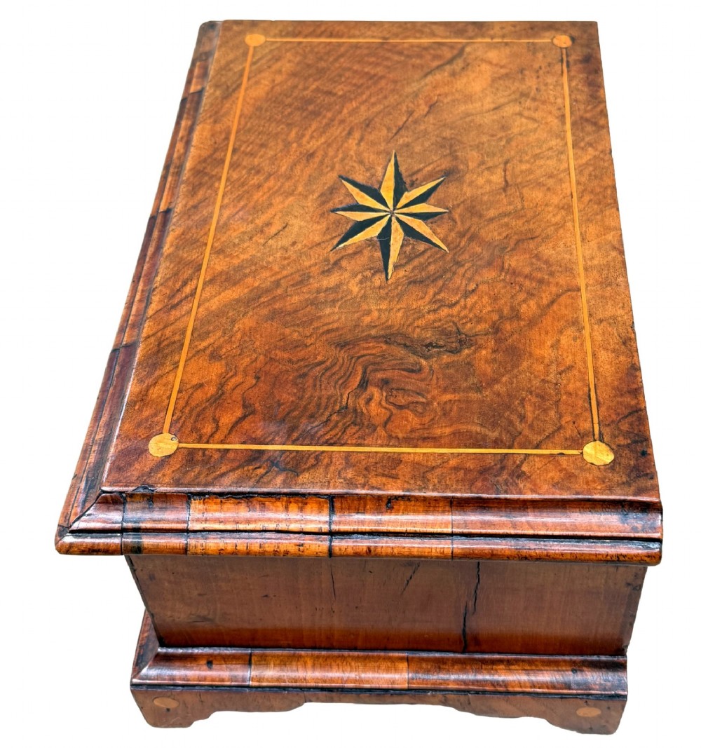 An early 18th-century walnut miniature chest featuring two drawers, star marquetry inlay, crossbanding, brass drop ring handles, and bracket feet. View VI