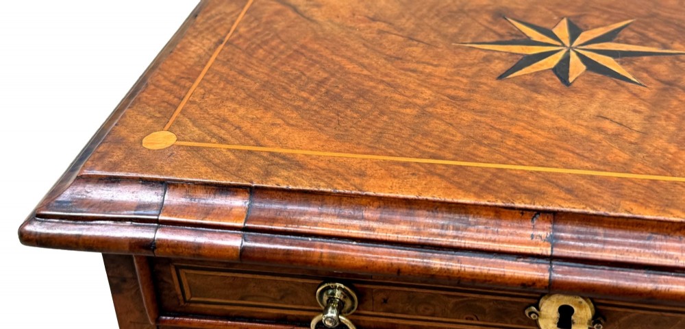 An early 18th-century walnut miniature chest featuring two drawers, star marquetry inlay, crossbanding, brass drop ring handles, and bracket feet. View VII