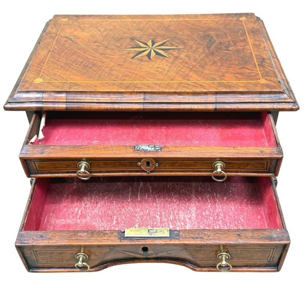 An early 18th-century walnut miniature chest featuring two drawers, star marquetry inlay, crossbanding, brass drop ring handles, and bracket feet. View VIII