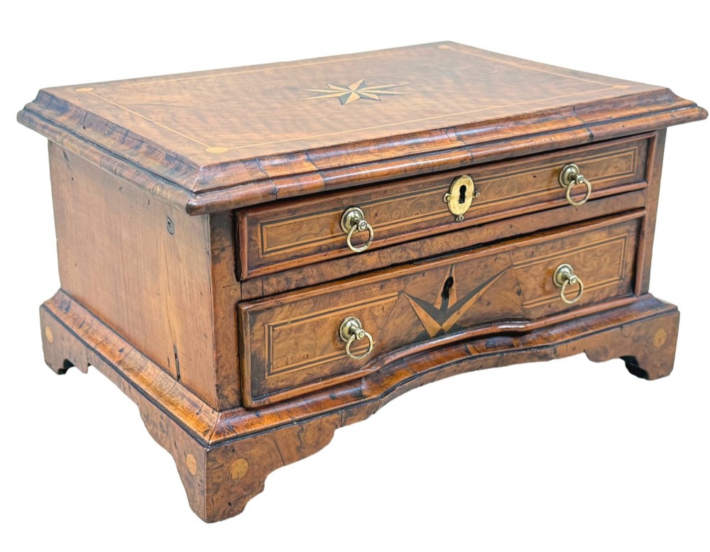 An early 18th-century walnut miniature chest featuring two drawers, star marquetry inlay, crossbanding, brass drop ring handles, and bracket feet. View X