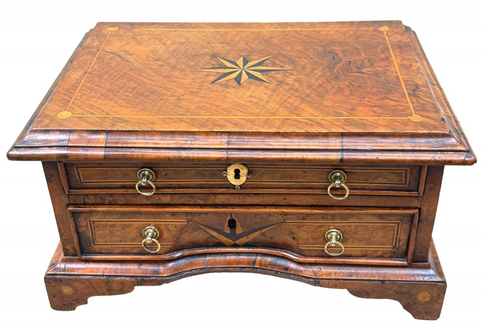 An early 18th-century walnut miniature chest featuring two drawers, star marquetry inlay, crossbanding, brass drop ring handles, and bracket feet. View XIII