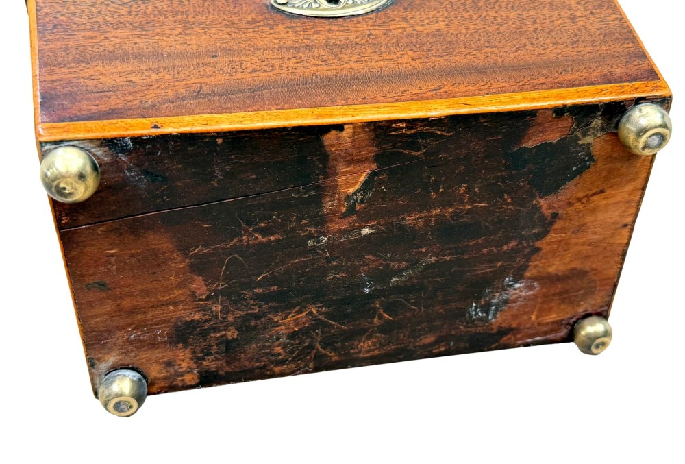 An eighteenth-century Georgian mahogany tea caddy featuring a sarcophagus shape, boxwood edging, an oval brass escutcheon, and brass ball feet. View IX