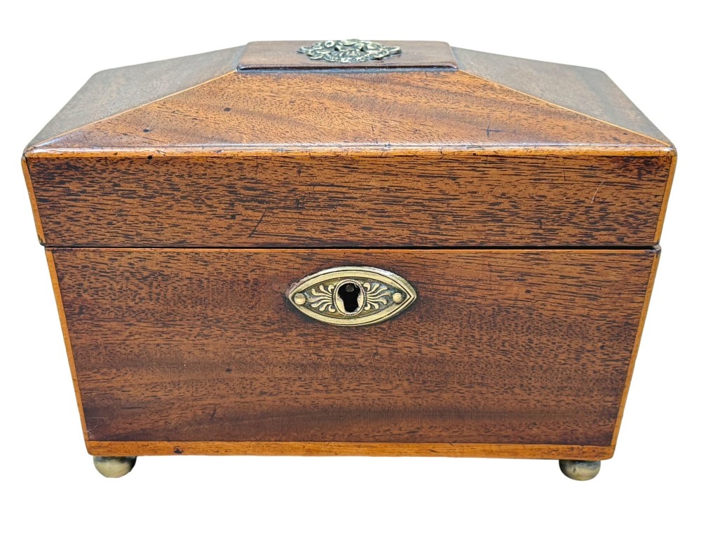 An eighteenth-century Georgian mahogany tea caddy featuring a sarcophagus shape, boxwood edging, an oval brass escutcheon, and brass ball feet. View X