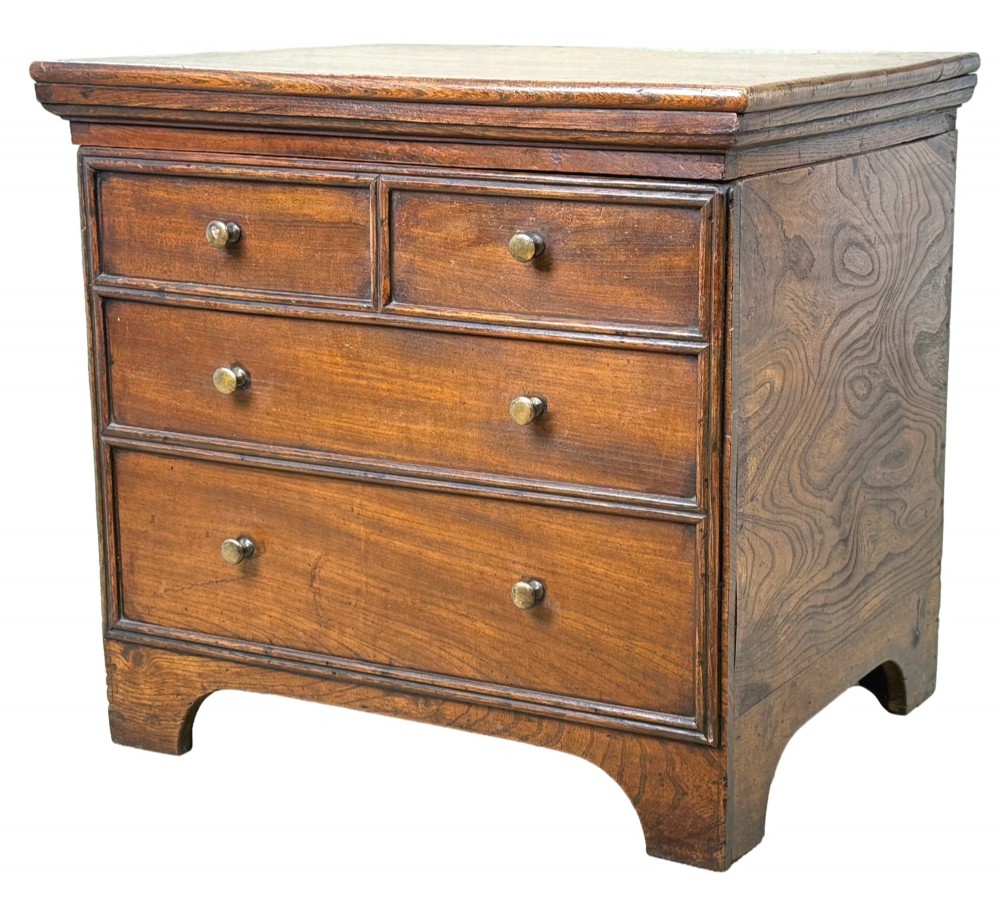 An 18th-century warm brown elm close stool designed as a small Georgian chest of drawers with bracket feet and brass handles.