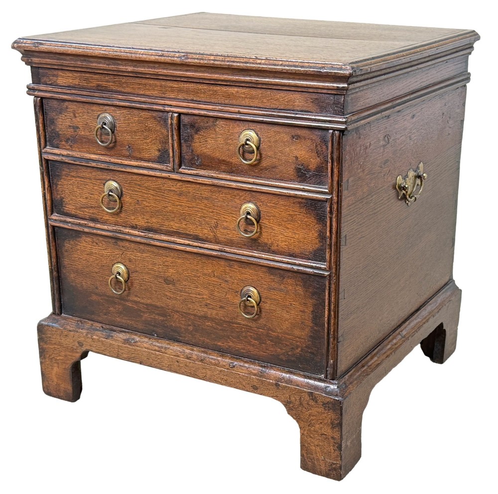An 18th-century dark oak close stool designed as a small chest with faux drawer fronts, brass ring handles, and bracket feet.