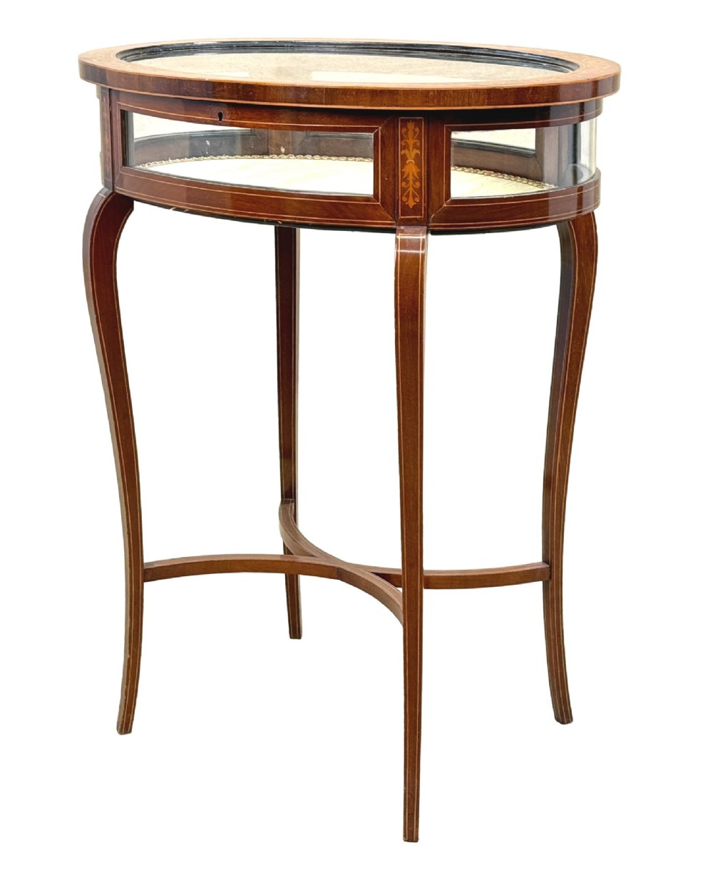 An oval late 19th-century mahogany bijouterie display table featuring glass side panels, inlaid floral marquetry, slender cabriole legs, and a cross stretcher.