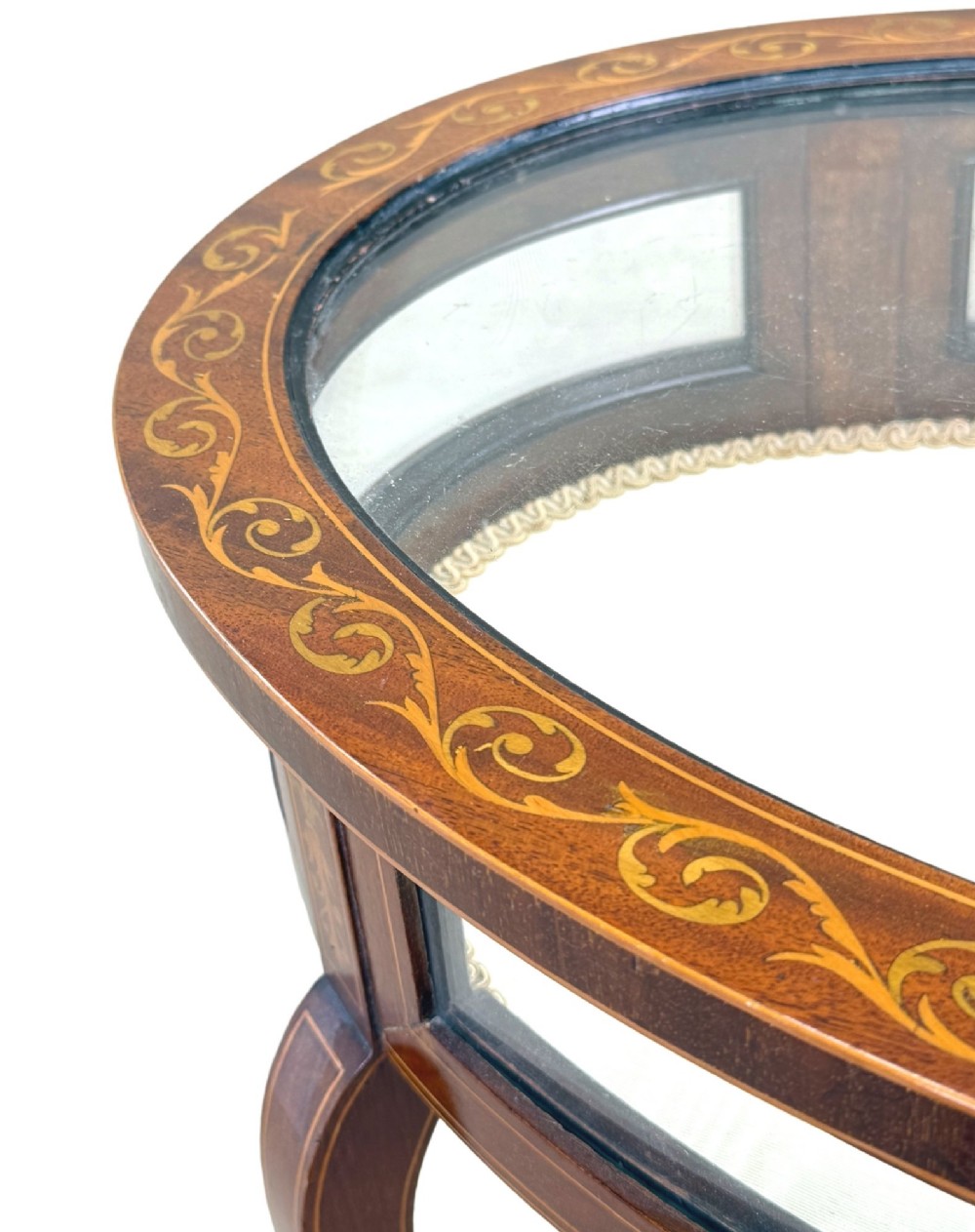 An oval late 19th-century mahogany bijouterie display table featuring glass side panels, inlaid floral marquetry, slender cabriole legs, and a cross stretcher. View III