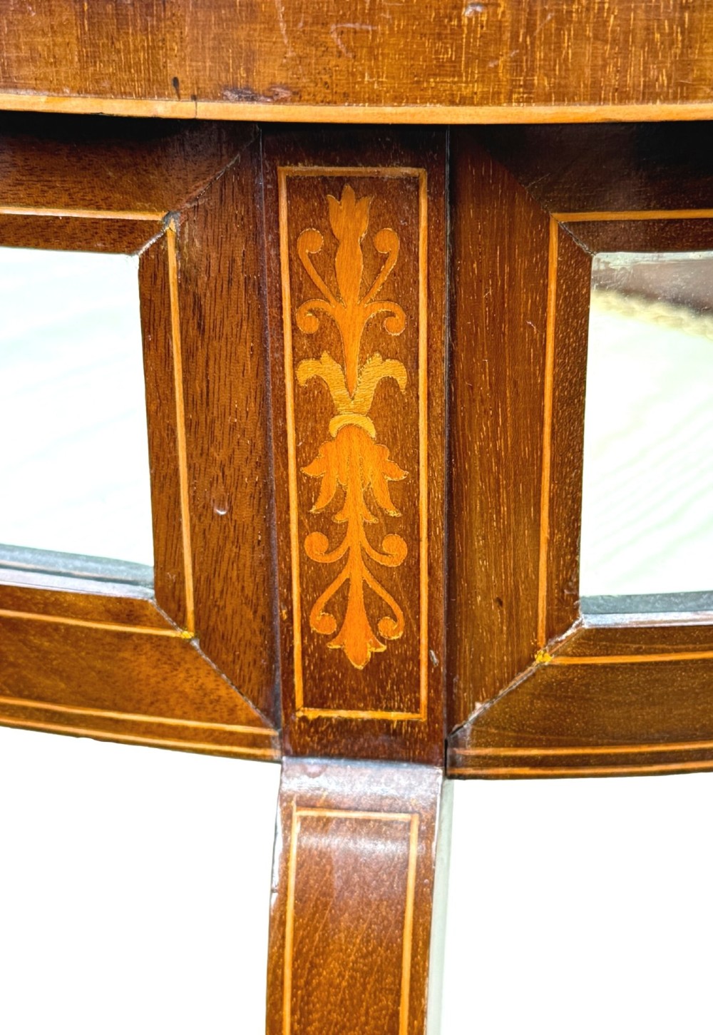 An oval late 19th-century mahogany bijouterie display table featuring glass side panels, inlaid floral marquetry, slender cabriole legs, and a cross stretcher. View VI
