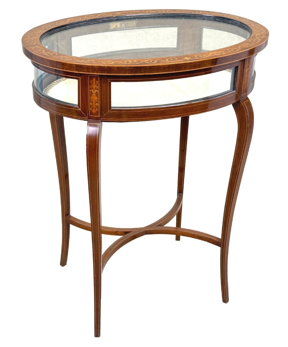 An oval late 19th-century mahogany bijouterie display table featuring glass side panels, inlaid floral marquetry, slender cabriole legs, and a cross stretcher. View VIII
