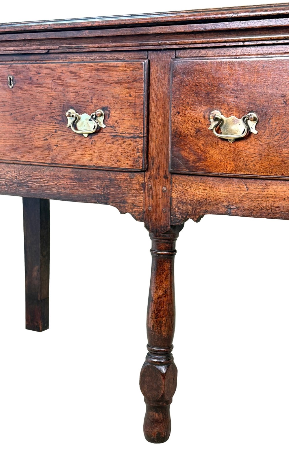 An early eighteenth-century oak dresser base featuring three drawers with brass drop handles, brass keyhole escutcheons, turned front legs, and a dark brown finish. View II