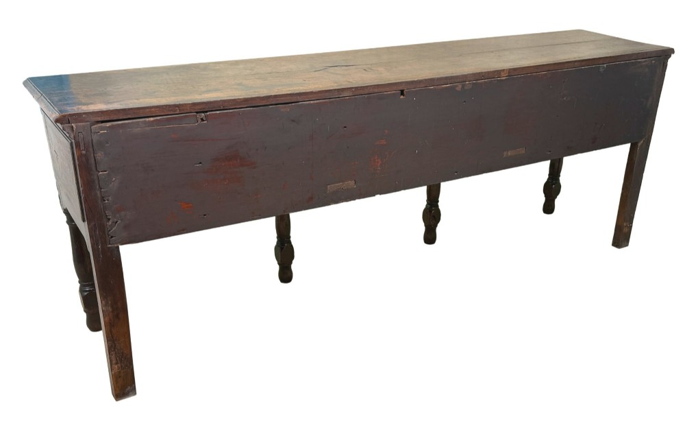 An early eighteenth-century oak dresser base featuring three drawers with brass drop handles, brass keyhole escutcheons, turned front legs, and a dark brown finish. View IX