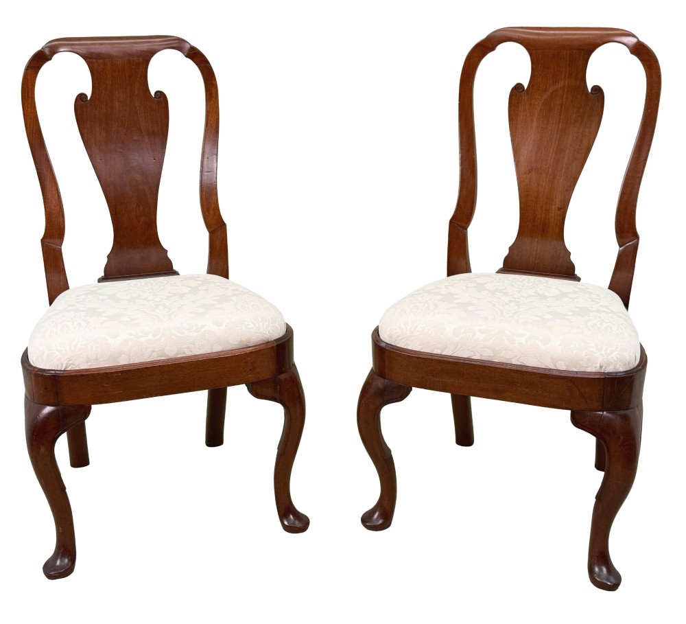 A pair of early 18th-century Queen Anne walnut side chairs featuring vase-shaped back splats, curved cabriole front legs, and cream upholstered drop-in seats. View X