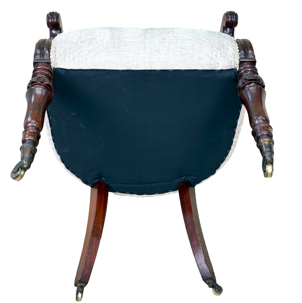 A 19th-century English Regency mahogany tub armchair with cream upholstery, scrolled armrests, turned legs, and brass castors. View IX
