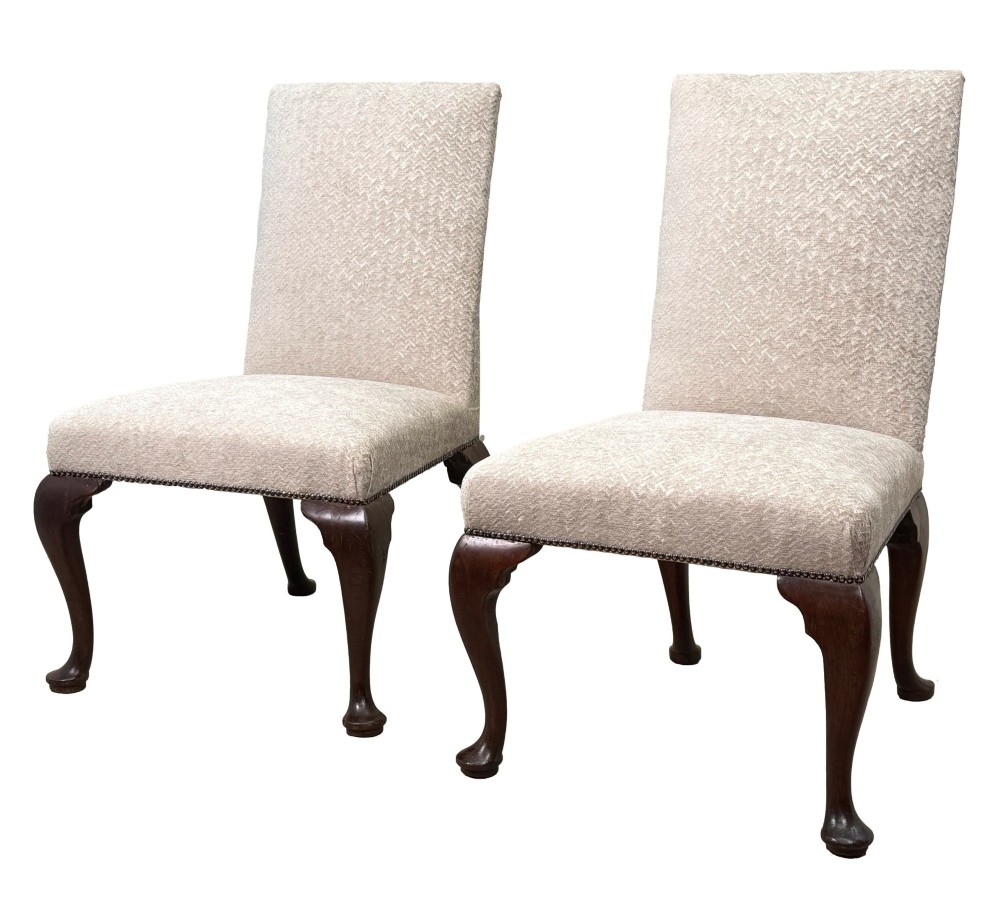 A pair of Georgian walnut side chairs featuring cream textured upholstery and carved cabriole legs ending in pad feet.