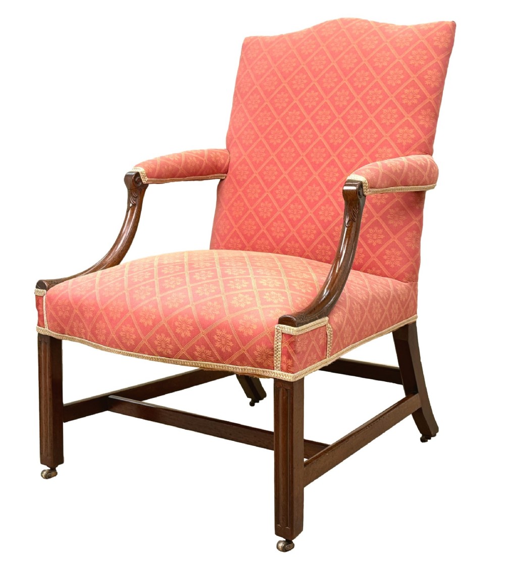 An 18th-century Georgian mahogany Gainsborough armchair with red patterned upholstery, curved carved arm supports, an H-stretcher frame, and brass castors.
