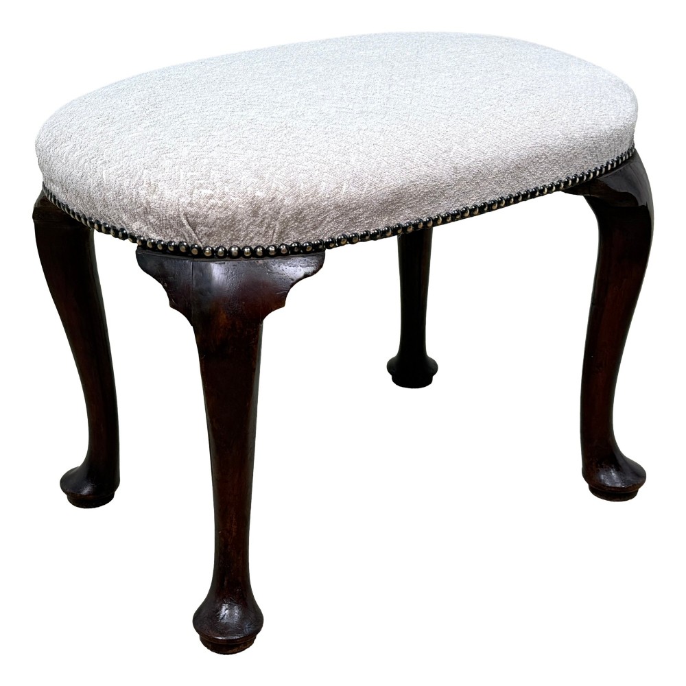 An early 18th-century George I walnut stool featuring an oval light grey upholstered seat trimmed with metal studs above four cabriole legs ending in pad feet. View VI