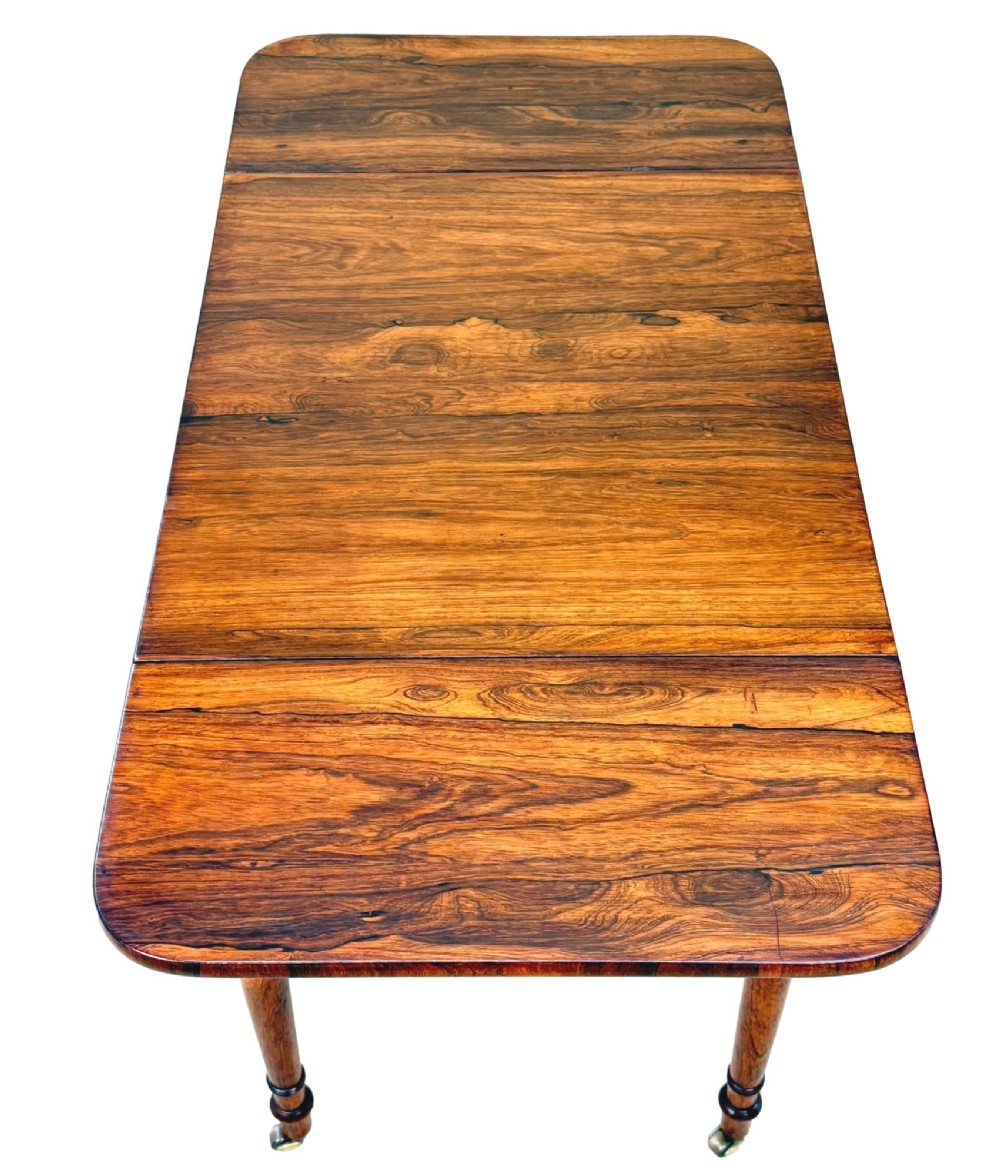 An early 19th-century Regency rosewood Pembroke table featuring extended drop leaves, turned legs on brass castors, and a single frieze drawer with brass knobs. View II