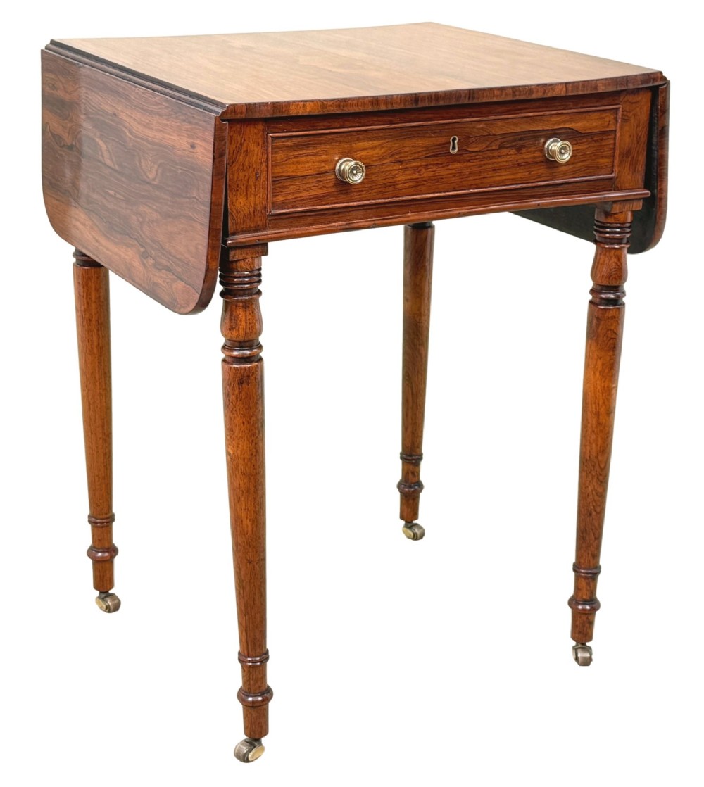 An early 19th-century Regency rosewood Pembroke table featuring extended drop leaves, turned legs on brass castors, and a single frieze drawer with brass knobs. View X