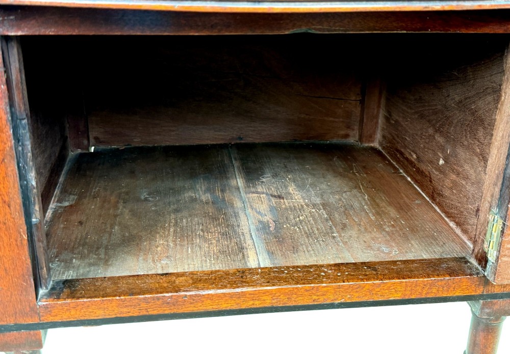 An early 19th-century Georgian mahogany side table featuring an oval top, single door cupboard with brass knob, turned legs, and an X-shaped cross stretcher. View VI