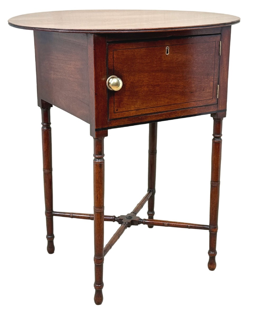 An early 19th-century Georgian mahogany side table featuring an oval top, single door cupboard with brass knob, turned legs, and an X-shaped cross stretcher. View VII
