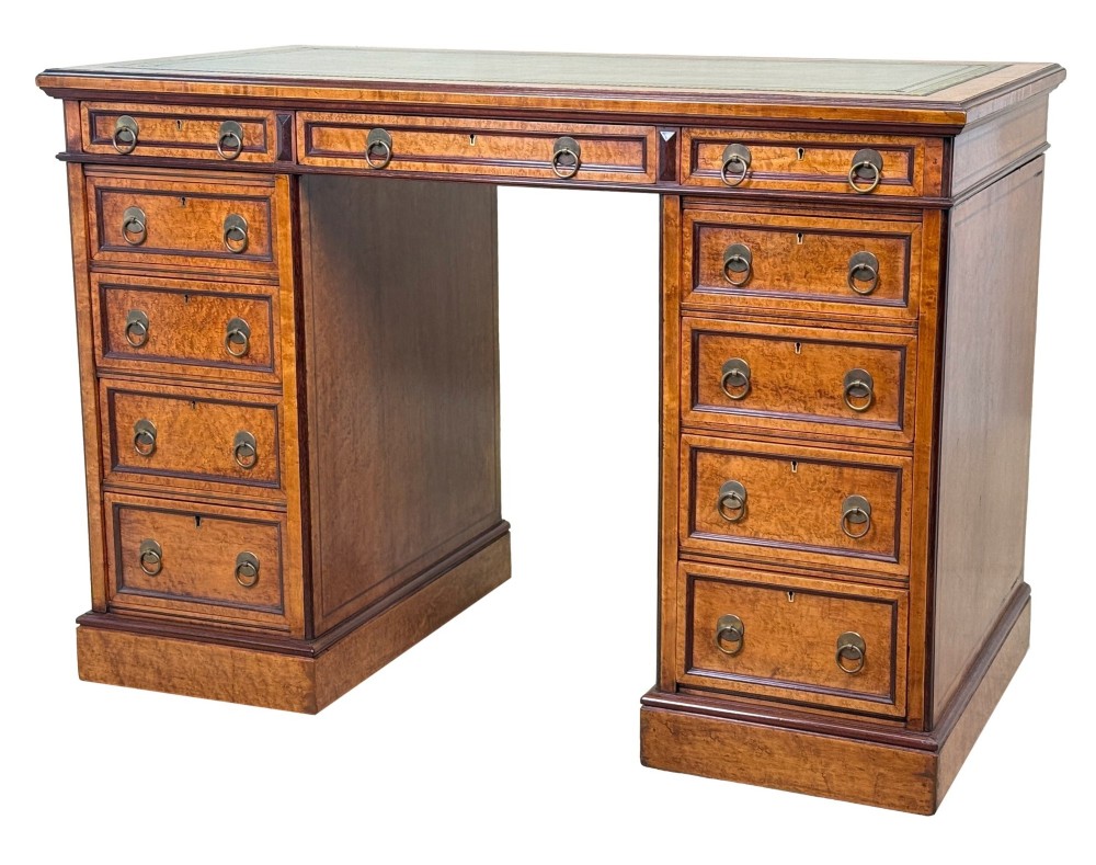 A mid-19th-century English birdseye maple pedestal desk featuring a green leather writing surface, multiple drawers with brass ring drop handles, and a plinth base.