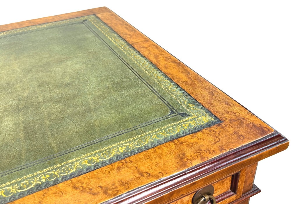 A mid-19th-century English birdseye maple pedestal desk featuring a green leather writing surface, multiple drawers with brass ring drop handles, and a plinth base. View VI