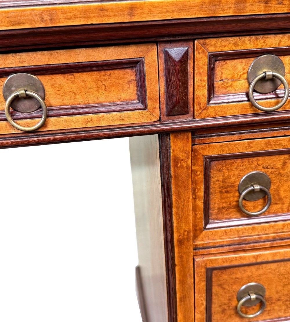 A mid-19th-century English birdseye maple pedestal desk featuring a green leather writing surface, multiple drawers with brass ring drop handles, and a plinth base. View VII