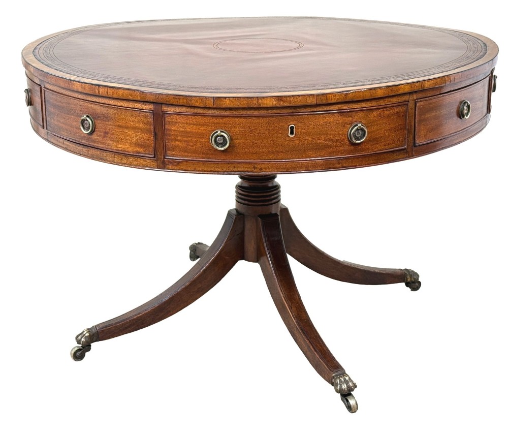 A circular Georgian mahogany drum table featuring a brown leather top, frieze drawers with brass ring handles, and a pedestal base with four splayed legs on brass paw castors.