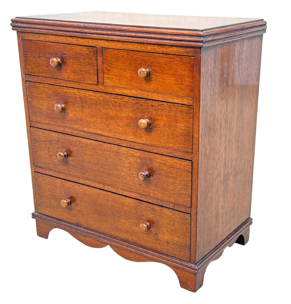 A miniature early nineteenth-century mahogany chest of drawers with two short over three long graduated drawers, turned wooden knobs, and a shaped apron base.