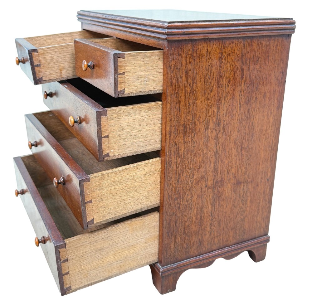 A miniature early nineteenth-century mahogany chest of drawers with two short over three long graduated drawers, turned wooden knobs, and a shaped apron base. View II