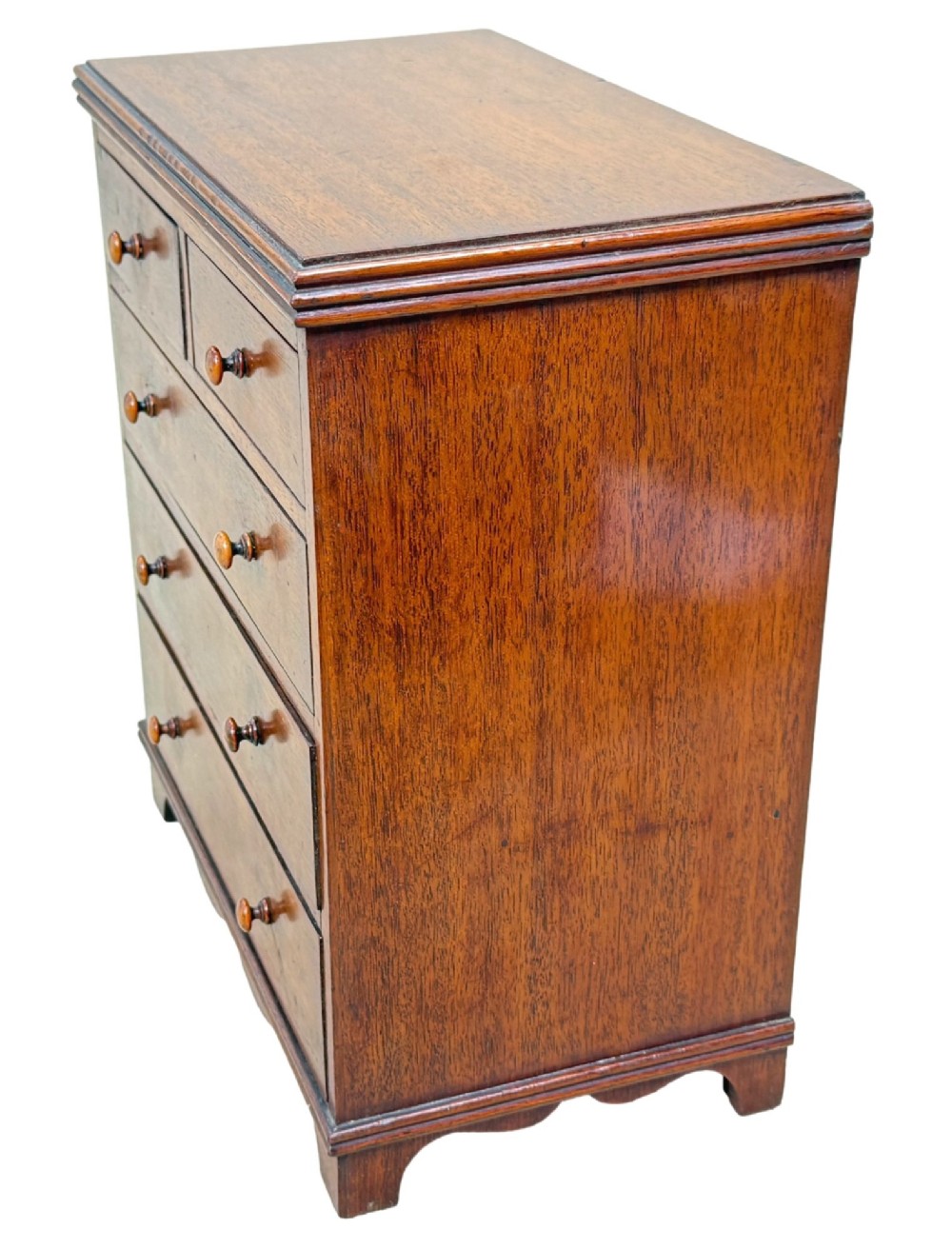 A miniature early nineteenth-century mahogany chest of drawers with two short over three long graduated drawers, turned wooden knobs, and a shaped apron base. View V