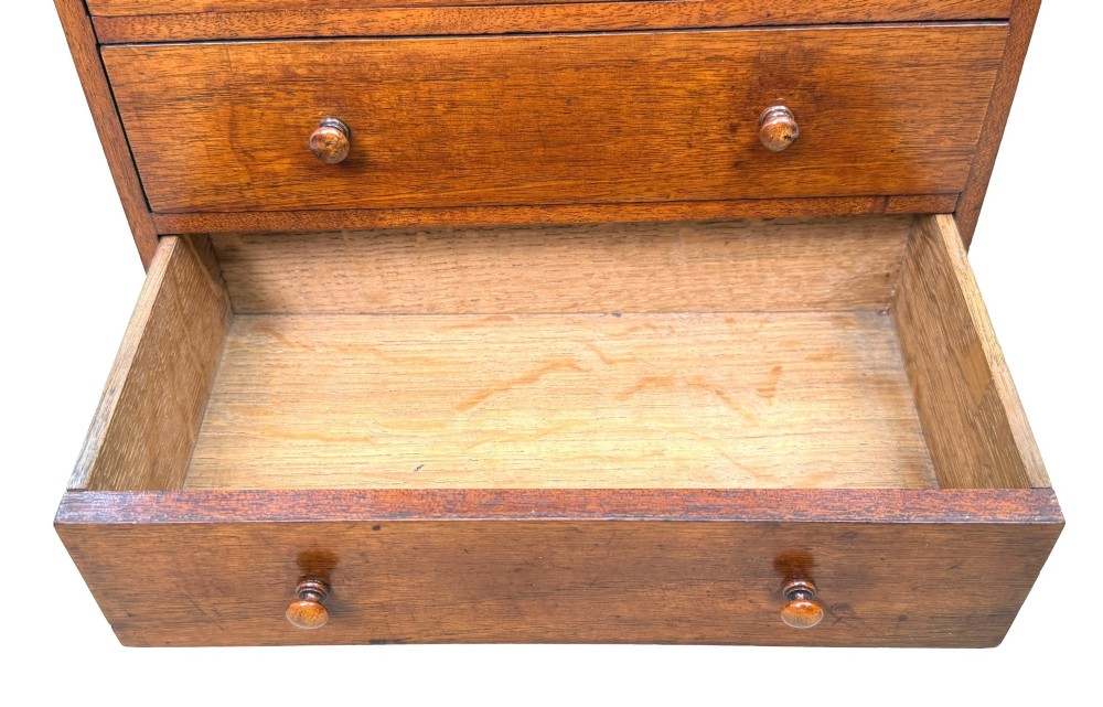 A miniature early nineteenth-century mahogany chest of drawers with two short over three long graduated drawers, turned wooden knobs, and a shaped apron base. View VI