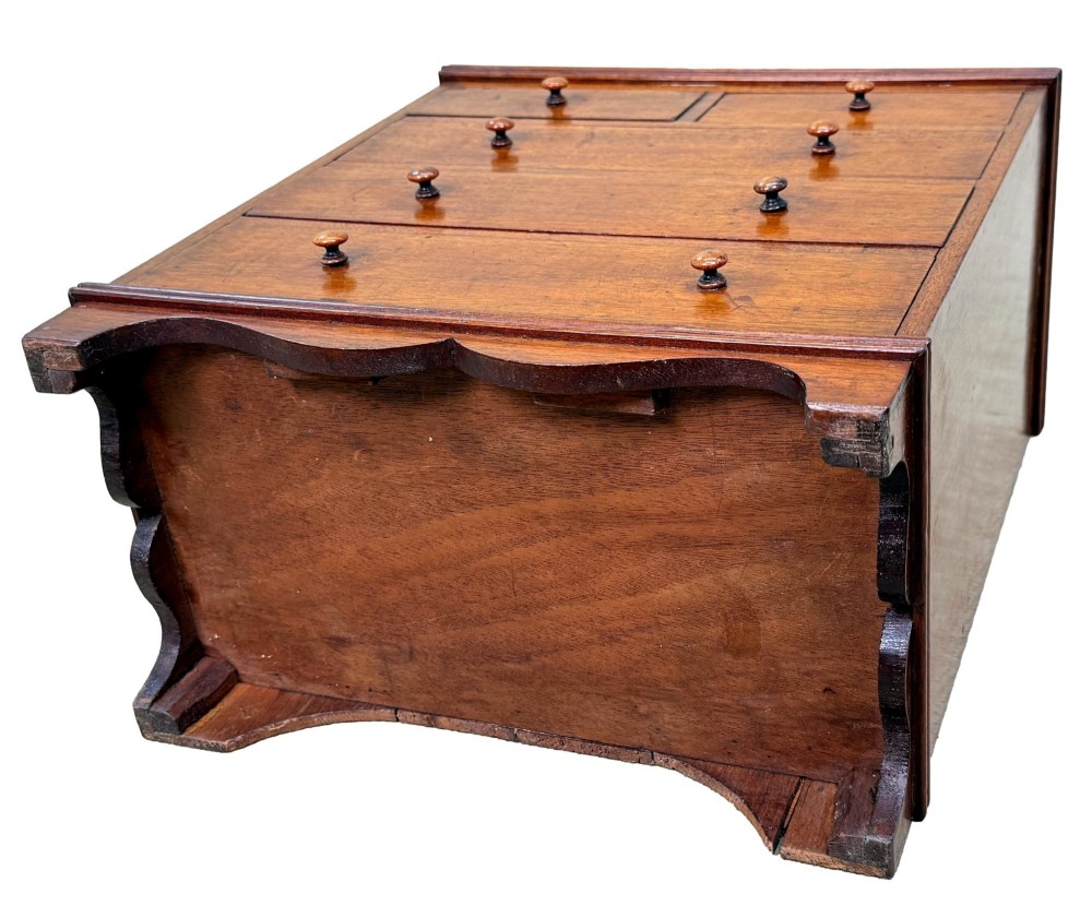 A miniature early nineteenth-century mahogany chest of drawers with two short over three long graduated drawers, turned wooden knobs, and a shaped apron base. View VII