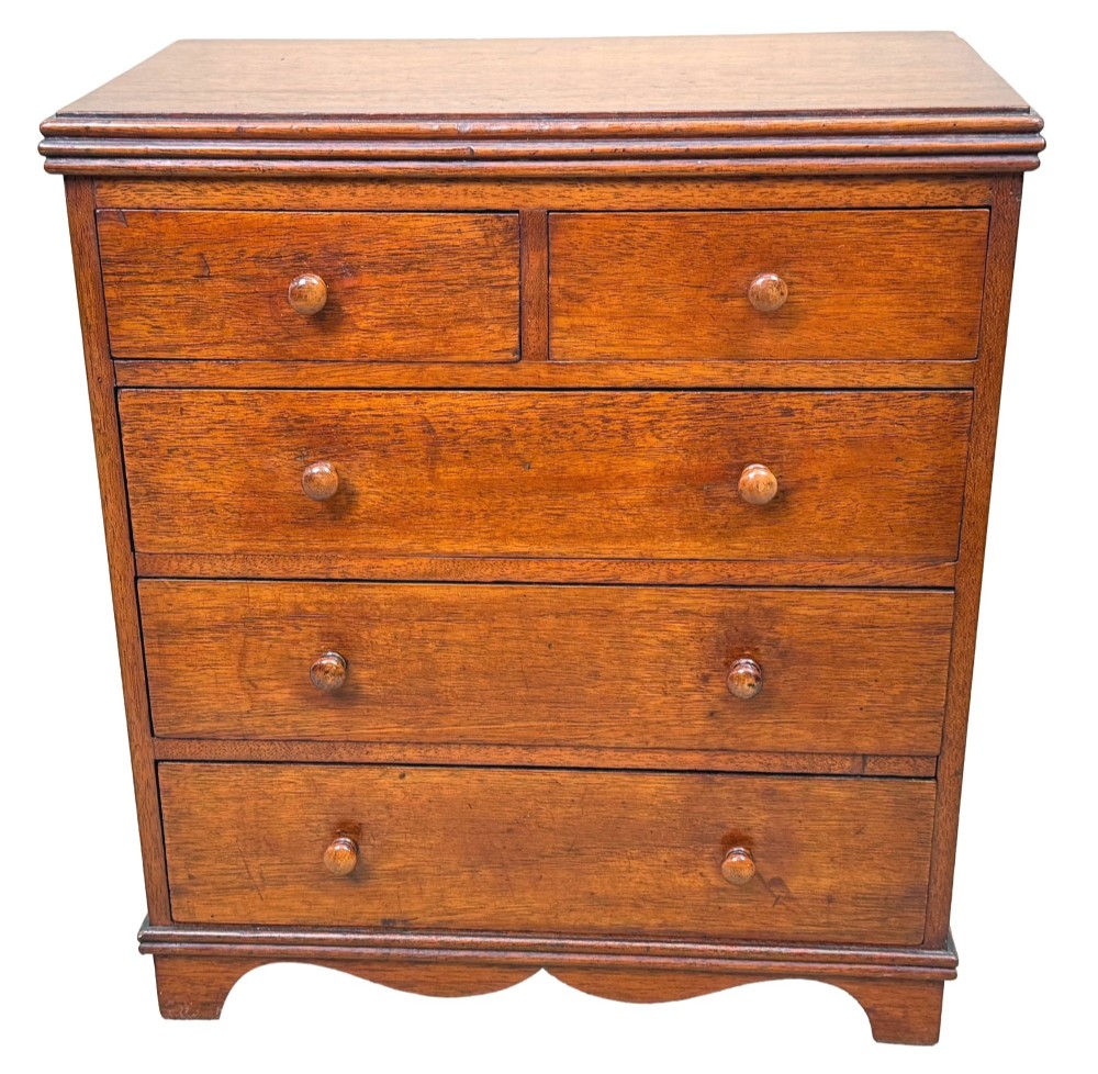 A miniature early nineteenth-century mahogany chest of drawers with two short over three long graduated drawers, turned wooden knobs, and a shaped apron base. View IX