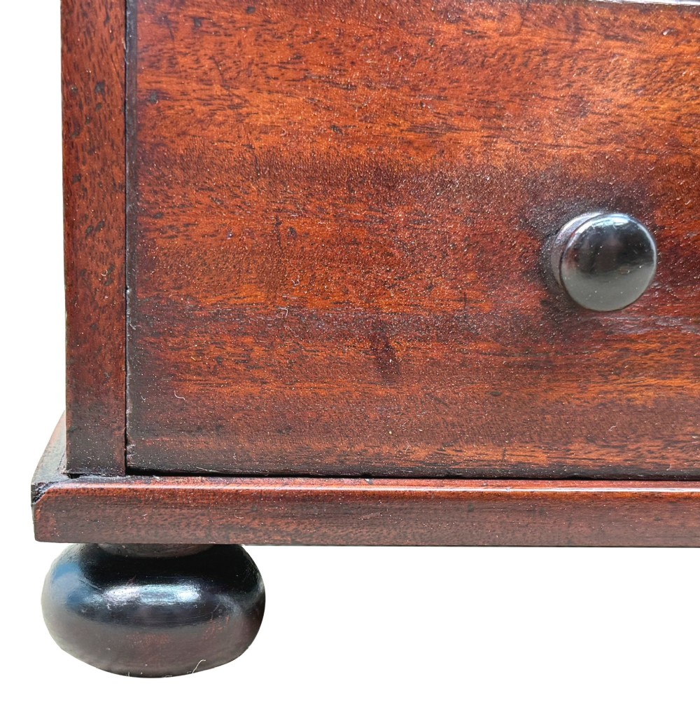 A mid-nineteenth-century miniature mahogany chest of drawers featuring two short over three long drawers, turned dark knobs, and bun feet. View III