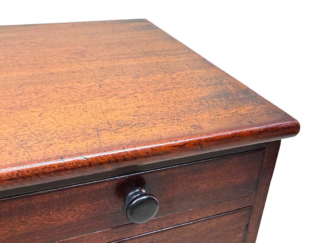 A mid-nineteenth-century miniature mahogany chest of drawers featuring two short over three long drawers, turned dark knobs, and bun feet. View IV