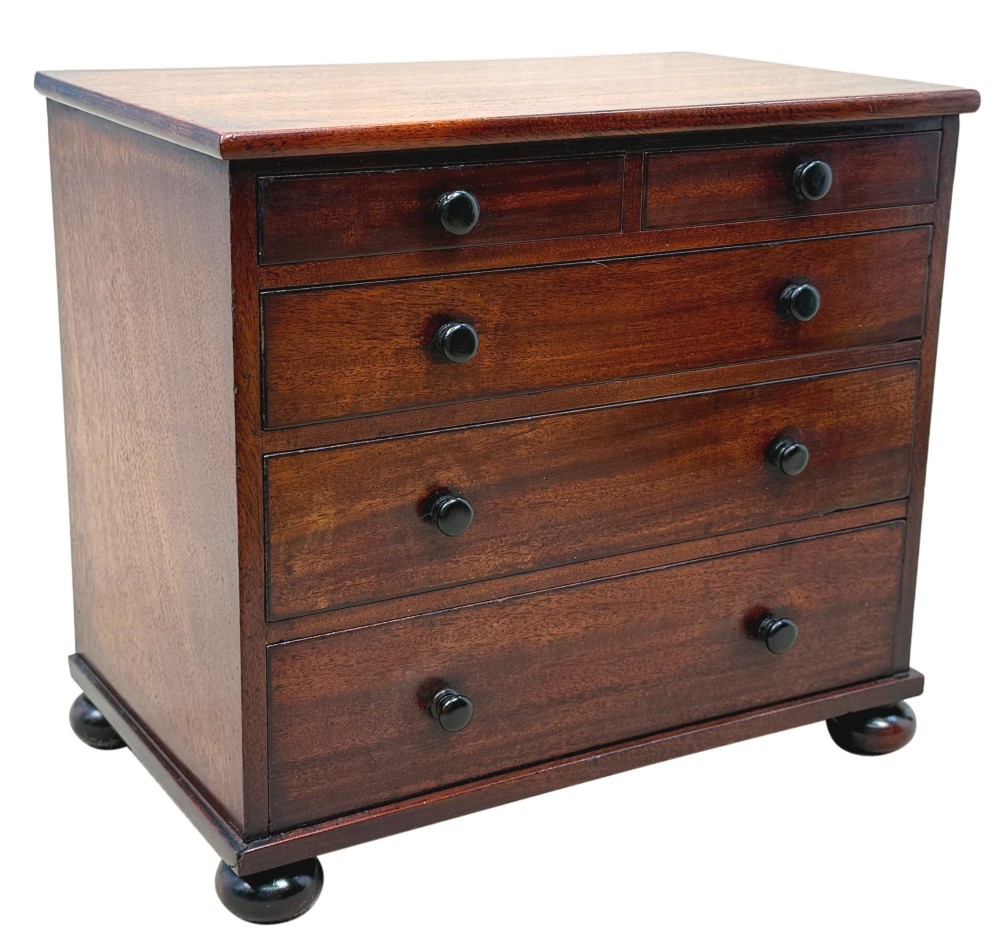 A mid-nineteenth-century miniature mahogany chest of drawers featuring two short over three long drawers, turned dark knobs, and bun feet. View VII