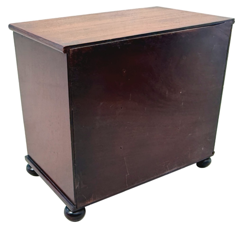 A mid-nineteenth-century miniature mahogany chest of drawers featuring two short over three long drawers, turned dark knobs, and bun feet. View VIII