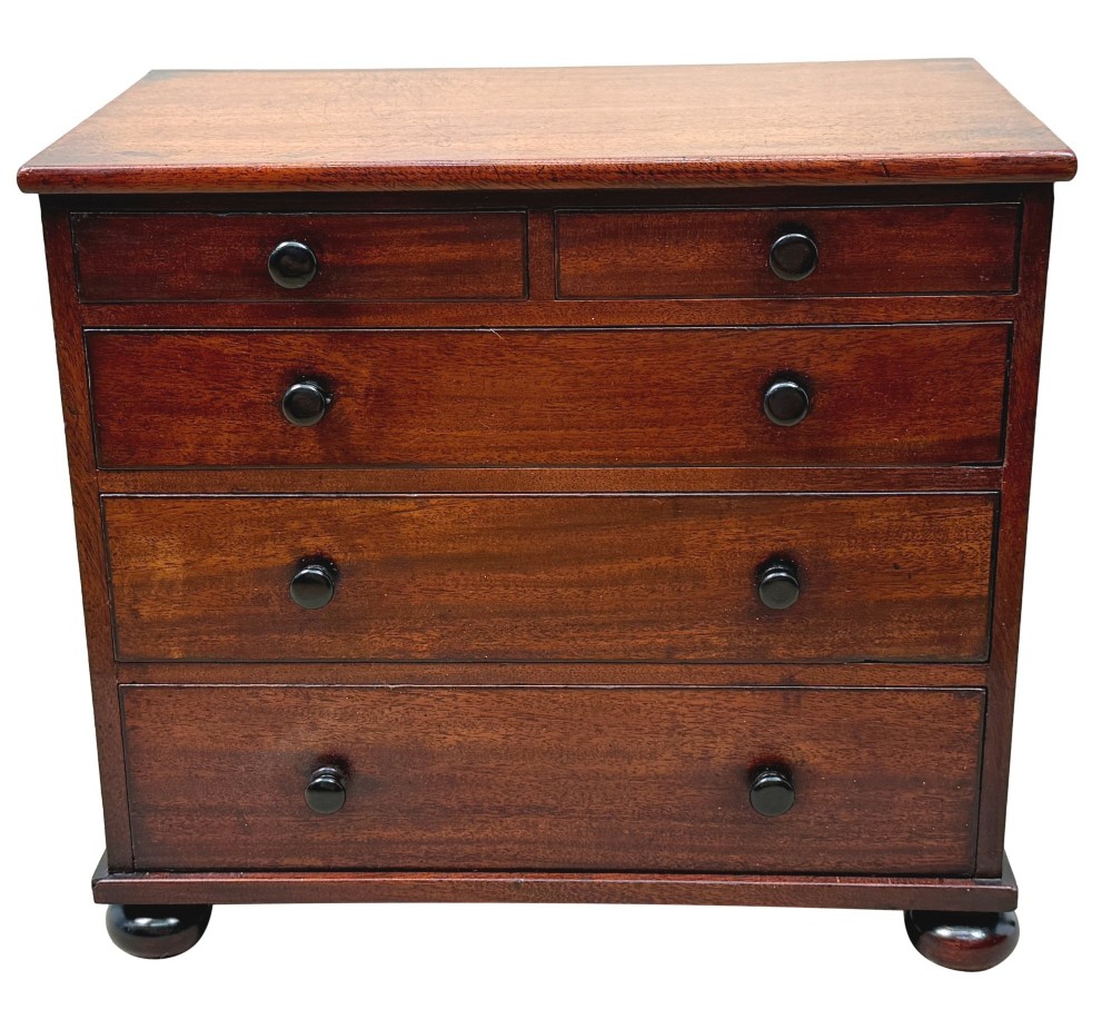 A mid-nineteenth-century miniature mahogany chest of drawers featuring two short over three long drawers, turned dark knobs, and bun feet. View X
