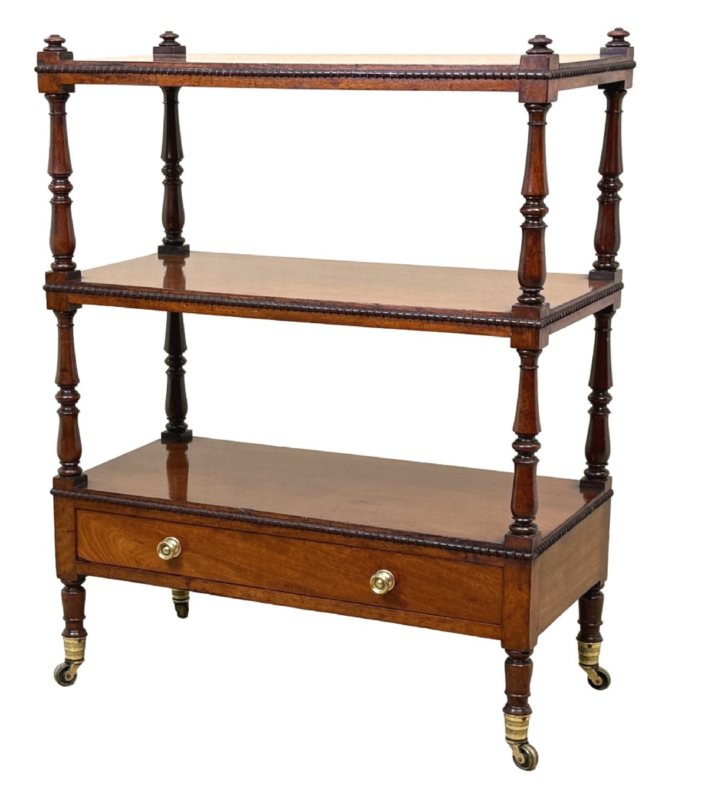 An early nineteenth-century Regency mahogany three-tiered etagere whatnot with turned supports, finials, a lower drawer, and brass castors.