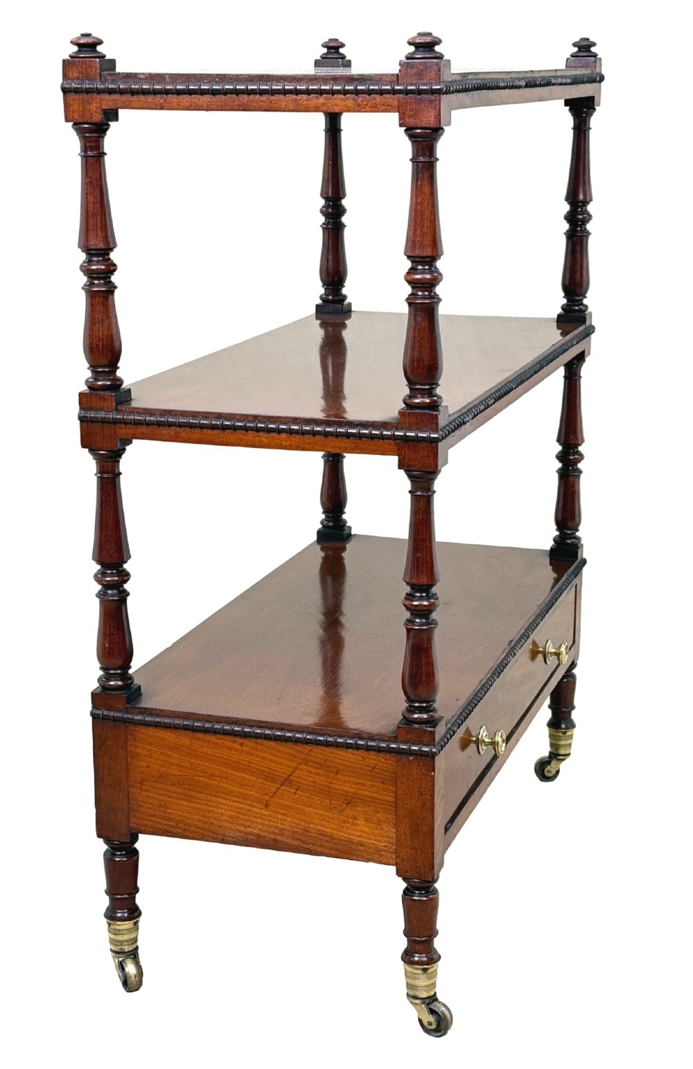 An early nineteenth-century Regency mahogany three-tiered etagere whatnot with turned supports, finials, a lower drawer, and brass castors. View II