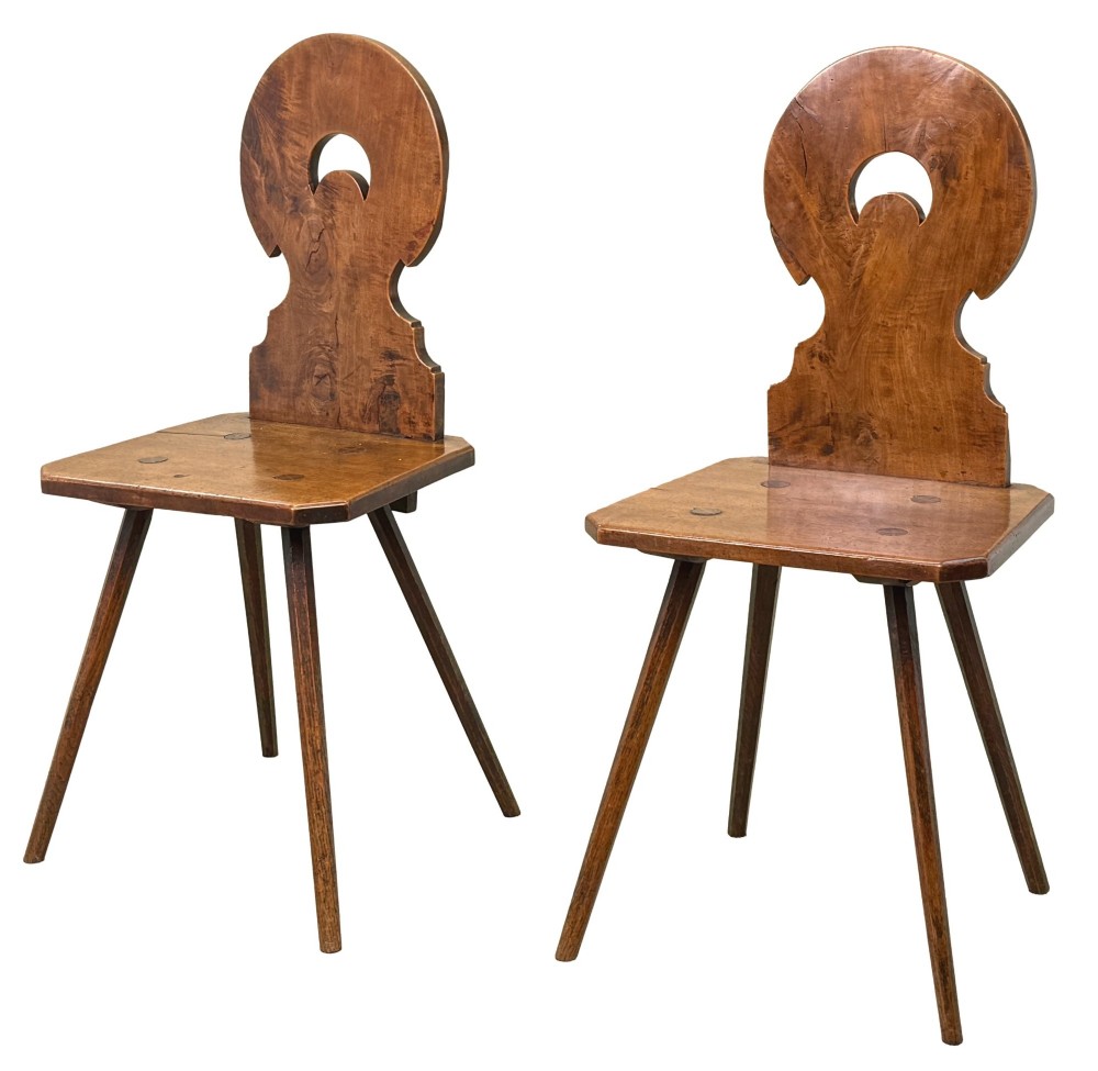 A pair of mid-19th-century Swiss escabelle chairs crafted from warm brown fruitwood, featuring circular carved backrests with cut-out motifs and four splayed tapered legs.