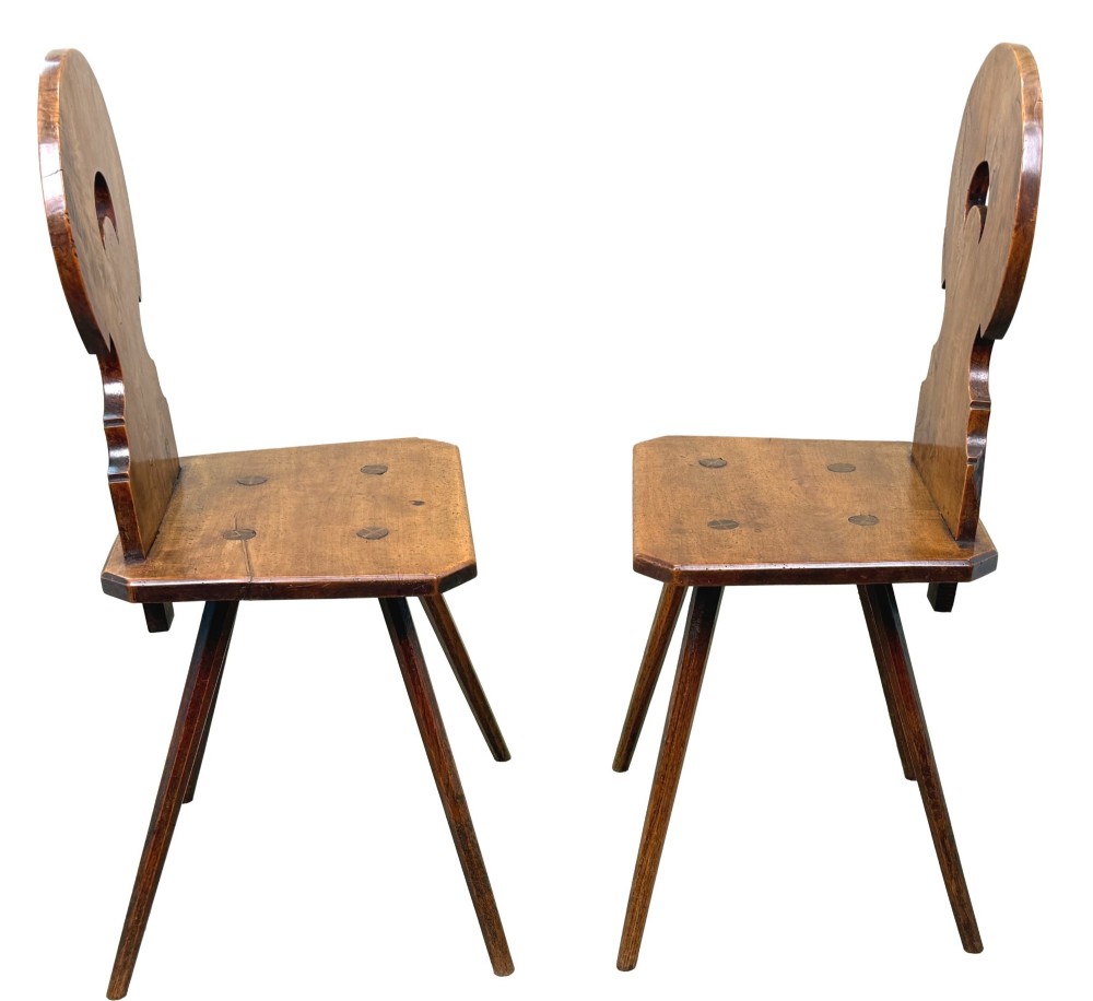 A pair of mid-19th-century Swiss escabelle chairs crafted from warm brown fruitwood, featuring circular carved backrests with cut-out motifs and four splayed tapered legs. View II