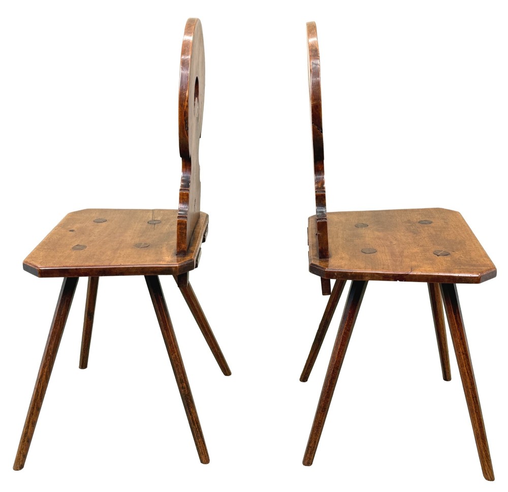 A pair of mid-19th-century Swiss escabelle chairs crafted from warm brown fruitwood, featuring circular carved backrests with cut-out motifs and four splayed tapered legs. View III
