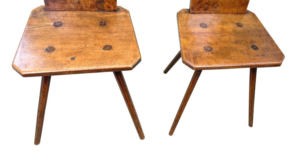 A pair of mid-19th-century Swiss escabelle chairs crafted from warm brown fruitwood, featuring circular carved backrests with cut-out motifs and four splayed tapered legs. View VI