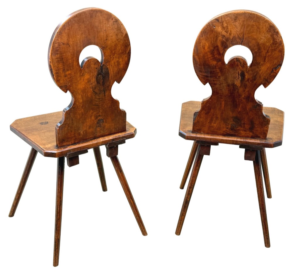A pair of mid-19th-century Swiss escabelle chairs crafted from warm brown fruitwood, featuring circular carved backrests with cut-out motifs and four splayed tapered legs. View VII