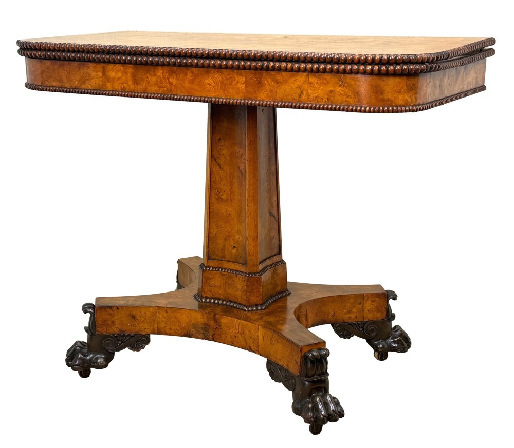 An early 19th-century Regency period pollard oak fold-over tea table featuring a rectangular top, beaded edging, a central pedestal support, and a quadripartite base resting on carved claw feet.