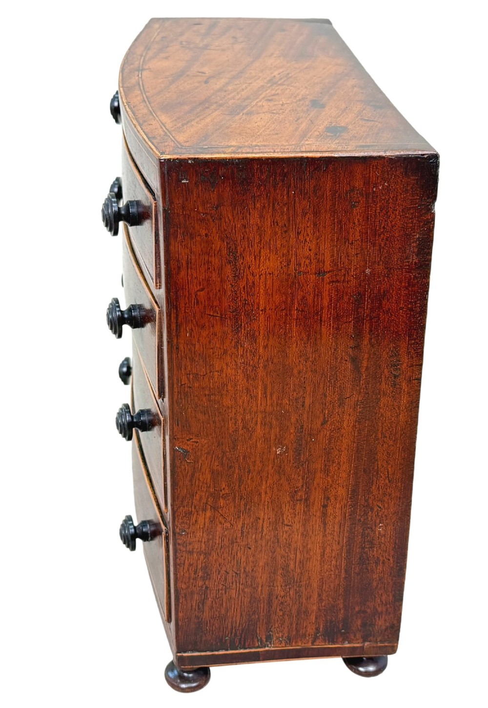 An 18th-century Georgian mahogany miniature bowfront chest of drawers featuring boxwood inlay, four graduated drawers with turned wooden knobs, and low bun feet. View VI