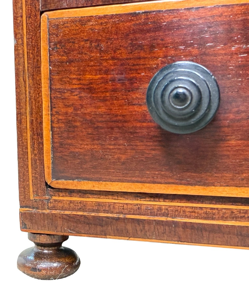 An 18th-century Georgian mahogany miniature bowfront chest of drawers featuring boxwood inlay, four graduated drawers with turned wooden knobs, and low bun feet. View VII
